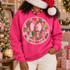 Pink smiley face DTF transfer filled with hand-painted pink, green, teal, and cream Christmas trees and decorative bows Shown on a Heliconia crewneck sweatshirt.