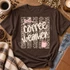 Coffee Weather DTF transfer with cream brush-script lettering over a distressed leopard print background, pink bow, and pink steaming coffee mug Shown on a Espresso t-shirt.