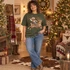 Cowboy swinging a lasso while riding Rudolick the reindeer DTF transfer, featuring western gear, studded saddle, and jingle-bell collar in illustrated style Shown on a Military Green crewneck sweatshirt.