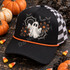 Spooky-cute ghost DTF transfer with glitter-style stitching, black lace spiderwebs, bats, stars, and orange daisy flowers in a Halloween patch design Shown on a Black front panel and bill with an orange rope accent, black-and-white checkered mesh back trucker hat.