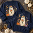 Whimsical floral ghost DTF transfer holding a wildflower bouquet with pumpkins, autumn flowers, and a crescent moon Shown on a Indigo Blue crewneck sweatshirt.