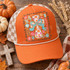 Give Thanks to the Lord Psalm 136:1 fall DTF transfer with pumpkin plaid cross, teal ribbon bow, and pink, orange, and blue florals Shown on a burnt pumpkin orange front panel with cream and tan checkered mesh back trucker hat.