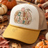 Gobble Till You Wobble DTF transfer with patchwork pumpkin design, bubble letters in fall-toned patterns, pink stem, and gold curly vine Shown on a Ivory front panel with mustard bill and tan mesh back trucker hat.
