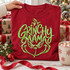 Grinchy Mama DTF transfer with green sequin-inspired script lettering shaped into a sly grinning Grinch-like face on a red shirt Shown on a Crimson t-shirt.
