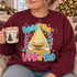 Behold The Lamb of God nativity DTF transfer with baby Jesus in a manger, Star of Bethlehem, lambs, and scalloped pink striped border Shown on a Maroon crewneck sweatshirt.