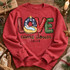 LOVE came down nativity DTF transfer with baby Jesus in a manger inside patterned block letters and Luke 2:11 scripture script Shown on a Heather Scarlet Red crewneck sweatshirt.