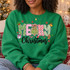 Merry Christmas DTF transfer with mixed-pattern block letters, a hand-drawn Christmas tree, holly, gingerbread man, gift box, candy cane, stocking, jingle bells, and red and green snowflakes on a red shirt Shown on a Irish Green crewneck sweatshirt.