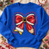 Teaching Is A Work Of Heart DTF transfer with a yarn-textured Christmas bow, white fur trim, gold buckle center, and pencil-tip tail surrounded by red script text Shown on a Royal crewneck sweatshirt.