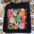 Colorful 'Merry' Christmas DTF transfer with gingerbread man, candy cane, Christmas tree, wreath, and ornament on a confetti background Shown on a Black crewneck sweatshirt.
