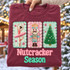 Nutcracker Season DTF transfer with yarn-embroidered-look ballerina, crowned nutcracker soldier, and Christmas tree patches on candy-striped backgrounds and chenille lettering Shown on a Wine t-shirt.