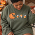 Pac-Man style jack-o-lantern DTF transfer chasing candy corn pieces and dots across an orange Halloween shirt Shown on a Military Green crewneck sweatshirt.