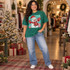 Cheerful waving snowman DTF transfer wearing a red Santa hat, mittens, and scarf on a teal and pink splatter background with snowflakes and glitter dots Shown on a Emerald t-shirt.