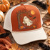 Cream-colored ghost swinging from a tree branch DTF transfer with glowing orange moon, bats, and autumn pumpkins Shown on a burnt orange front panel, cream rope and bill, white mesh back trucker hat.