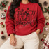 Frosty Season DTF transfer with cartoon snowman in top hat peeking through chunky bubble letters, snowflakes, and brush-script lettering Shown on a Cherry Red crewneck sweatshirt.