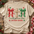 I Will Praise Him In Every Season Christmas DTF transfer with a rustic wooden cross, red and green chenille-style bows, and scattered snowflakes Shown on a Sandstone t-shirt.