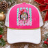 Holly Jolly nutcracker DTF transfer with pink and green nutcracker face, red bow, gold crown, in a pink scalloped frame over a mint polka-dot striped background with bold bubble lettering Shown on a Hot pink front panel, white pre-curved bill, white mesh back with gold rope trucker hat.