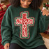 Jesus Saves distressed cross DTF transfer in red, green, and cream with weathered hand-drawn Christmas-inspired texture Shown on a Forest crewneck sweatshirt.