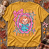Cutesy Horror DTF Transfers | Pastel Spooky Icons Collection, colorful pastel horror doll illustration with pink bows, stars, and a scalloped frame displayed on a mustard yellow T-shirt