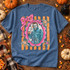 Cutesy Horror DTF Transfers | Pastel Spooky Icons Collection, pink bow and star-framed illustration of a masked horror character printed on a blue T-shirt surrounded by pumpkins and Halloween decor