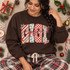 GIGI Christmas DTF transfer with chunky block letters in candy cane stripe, holly and berry, checkerboard, and leopard camo patterns, accented with holly, a jingle bell, and a candy cane, topped with red cursive gigi script Shown on a Dark Chocolate crewneck sweatshirt.