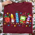 Christmas School Supplies DTF Transfer | Festive Crayon-Style Holiday Design, colorful smiling school supplies dressed as festive Christmas characters printed on a burgundy shirt, including a crayon, pencil, ruler, notebook, and marker