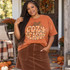 Cozy Season DTF Transfer | Gingham Plaid Fall Bubble Letter Design, orange fall T-shirt featuring large “Cozy Season” bubble lettering in orange-and-cream gingham plaid with autumn leaves and a pumpkin, modeled outdoors in a festive fall setting.