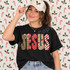 JESUS Christmas Patchwork DTF Transfer | Faith-Based Holiday Design, model wearing a black T-shirt featuring festive patchwork JESUS lettering in plaid, polka dot, floral, and striped Christmas patterns.