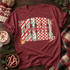 MIMI Christmas DTF transfer in block letters with candy cane stripes, holly berry, red checker, and leopard print patterns, accented with holly leaves, a jingle bell, and a candy cane, with mimi in red cursive script layered across the center Shown on a Wine t-shirt.