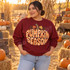 Pumpkin Season DTF Transfer | Gingham Pumpkin Fall Design, orange gingham pumpkin with autumn leaves and lettering displayed on a burgundy sweatshirt worn at a fall pumpkin patch.