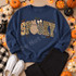 SPOOKY lettering DTF transfer with floral, camo, and leopard print fill, bow-topped checkered and polka-dot ghost characters, bats, and spiderwebs Shown on a Indigo Blue crewneck sweatshirt.