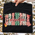 Grandma Christmas DTF transfer with block letters in candy cane, checkerboard, snowflake, and leopard patterns, topped with red cursive script and holly, bow, bell, and candy cane accents Shown on a Black t-shirt.