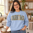 GRANDMA varsity letter DTF transfer with checkerboard, camo, leopard, polka dot, and floral patterns accented by cream bow ribbons Shown on a Light Blue crewneck sweatshirt.
