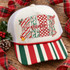 NANA Christmas DTF transfer with candy cane stripe, holly, checkerboard, and leopard print letters, holly leaves, a red bow, gold jingle bell, candy cane, and red script 'nana' overlay Shown on a ivory cream front panel with red and green striped bill and white mesh back trucker hat.