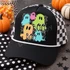 BOO Halloween DTF transfer featuring five patterned cartoon ghosts in teal, pink, green, and orange on a black and white speckled background with stars Shown on a black front panel with white rope and black-and-white checkered mesh back trucker hat.