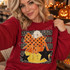 Candy corn DTF transfer with orange polka-dot bow and black stars on a dotted striped background Shown on a Cherry Red crewneck sweatshirt.
