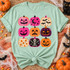 Retro block-print jack-o-lantern grid DTF transfer with nine pink, orange, and purple pumpkins featuring stars, moons, bats, a skeleton, and candy corn designs Shown on a Chalky Mint t-shirt.