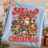 Merry Christmas DTF transfer with vintage-style Santa, reindeer, snowman, and gingerbread man peeking out of cracked bells, surrounded by candy canes, holly, and snowflakes Shown on a Ice Blue t-shirt.
