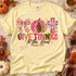 Give Thanks to the Lord DTF transfer with a patchwork checkered bow, plaid and polka dot pumpkin, colorful patterned cross, and Psalm 136:6 lettering Shown on a Butter t-shirt.