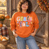 Grateful scrapbook-style word art DTF transfer with mixed-pattern paper-cut letters, pink ribbon bow, and stars in autumn pastel colors Shown on a Orange crewneck sweatshirt.
