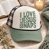 I Love Jesus & Naps DTF transfer in bold distressed sage green block lettering with cross and ampersand accents Shown on a ivory front panel, sage green bill, black-and-white checkered mesh back trucker hat.