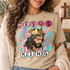 Jesus is King DTF transfer with painterly portrait of Jesus wearing a golden crown over a crown of thorns, teal brushstrokes, pink florals, and circle-letter text Shown on a Sandstone t-shirt.