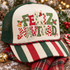 Feliz Navidad DTF transfer with oversized mixed-pattern lettering in leopard print, checkerboard, stripes, dots, and painted Christmas trees, accented by a gold bell, holly berries, a candy cane, and a snowman ornament Shown on a ivory front panel with red and green striped bill, forest green mesh back, twisted red-and-green rope trucker hat.