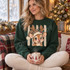 Cartoon fawn wearing a leopard-print Santa hat with cream fur trim and holly sprig, set against a rustic striped background DTF transfer Shown on a Forest crewneck sweatshirt.