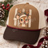 Cartoon fawn wearing a leopard-print Santa hat with cream fur trim and holly sprig, set against a rustic striped background DTF transfer Shown on a camel brown front panel, dark espresso bill, cream mesh back, burgundy rope trucker hat.