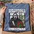 Have Yourself a Scary Little Christmas DTF transfer with Ghostface-style killer holding a knife and wrapped present at a snowy window with Christmas tree Shown on a Chambray t-shirt.