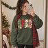SPED frosted-cookie-lettering DTF transfer with leopard print, checkerboard, and mini Christmas tree patterns surrounded by candy cane, holly, paint palette, book, pencil and ruler doodles Shown on a Military Green crewneck sweatshirt.
