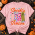 Spooky Season DTF transfer featuring four patterned ghosts in pink hearts, rainbow polka dots, floral, and checkerboard designs with orange script lettering and Halloween doodles Shown on a Blossom t-shirt.