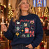 True Story nativity DTF transfer with hand-drawn sticker-sheet grid featuring the holy family, sheep, donkey, church, angel, manger, star of Bethlehem, cross, empty tomb, Christmas tree, and polka-dot bow framed by scribbly borders and snowflakes Shown on a Sapphire crewneck sweatshirt.