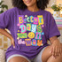 Better Days Are On The Way DTF transfer with colorful paper-collage lettering, a smiley face, stars and flowers Shown on a Grape t-shirt.