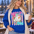 Let It Snow DTF transfer with a smiling patchwork snowman in a pink and teal striped hat and scarf, framed by a gold-glitter-style scalloped medallion with snowflakes and stars Shown on a Royal crewneck sweatshirt.